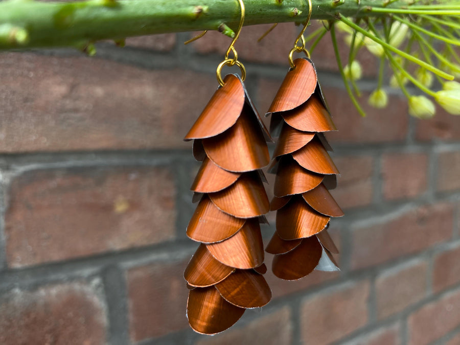 copper coloured cascade earrings made from upcycled nespresso capsule aluminium on a brick wall background