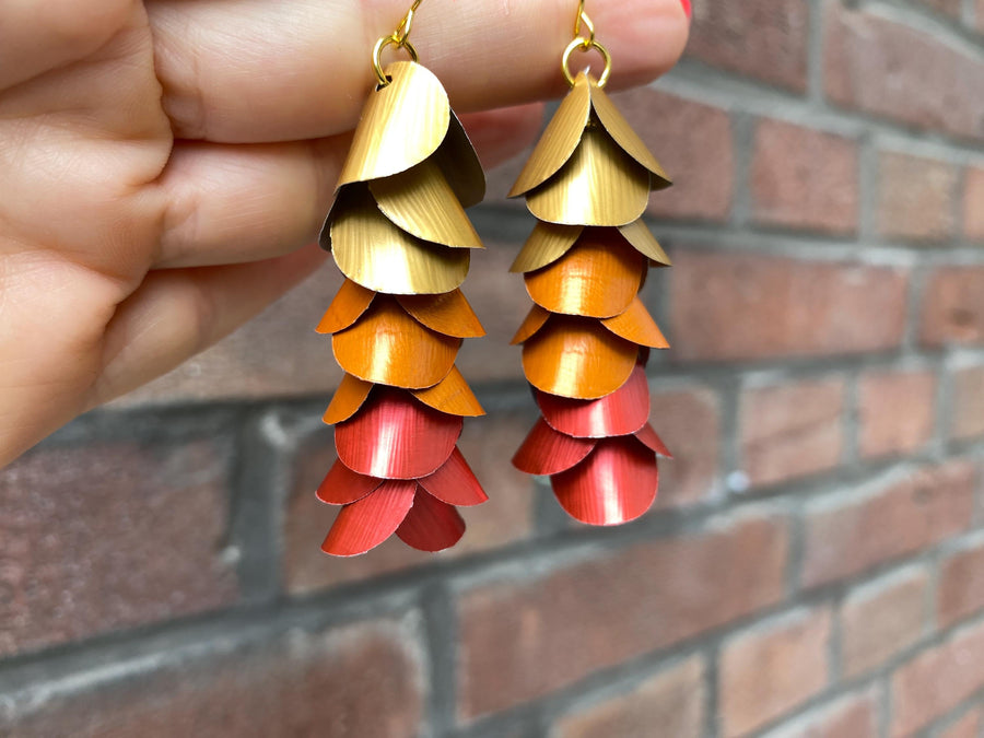 gold orange red cascade earrings made from upcycled nespresso capsules on a brick wall background