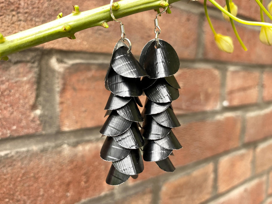a pair of black, cascading aluminium earrings made from upcycled nespresso capsules on a brick wall background