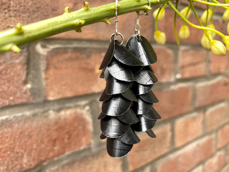 a pair of black, cascading aluminium earrings made from upcycled nespresso capsules on a brick wall background