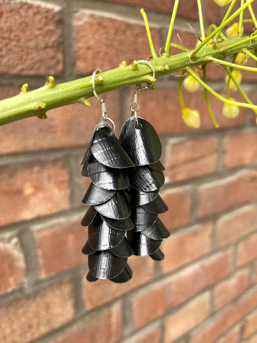 a pair of black, cascading aluminium earrings made from upcycled nespresso capsules on a brick wall background