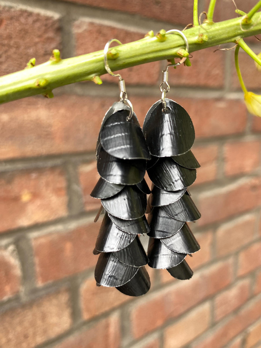 a pair of black, cascading aluminium earrings made from upcycled nespresso capsules on a brick wall background