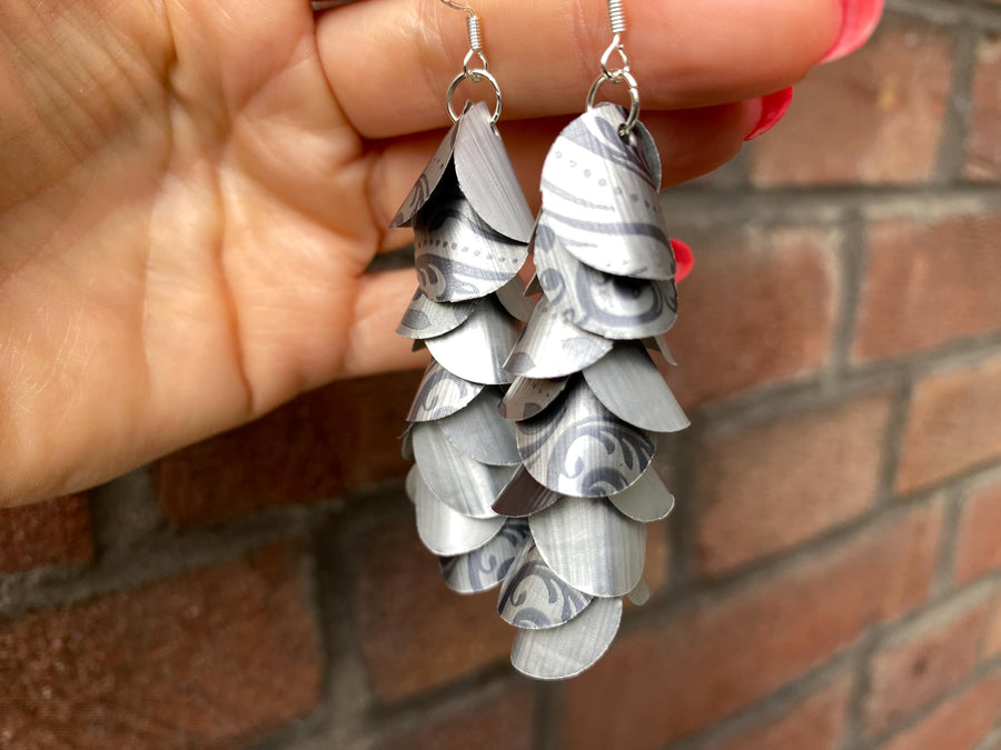 silver coloured cascade earrings made from upcycled nespresso capsules on a brick wall background