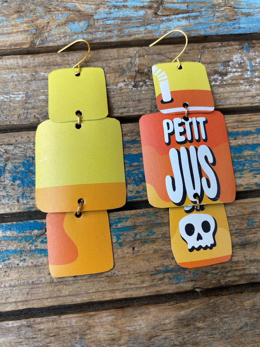 pair of yellow orange, asymmetric geometric earrings with text and skull design made from an upcycled beer can on a rustic wooden background