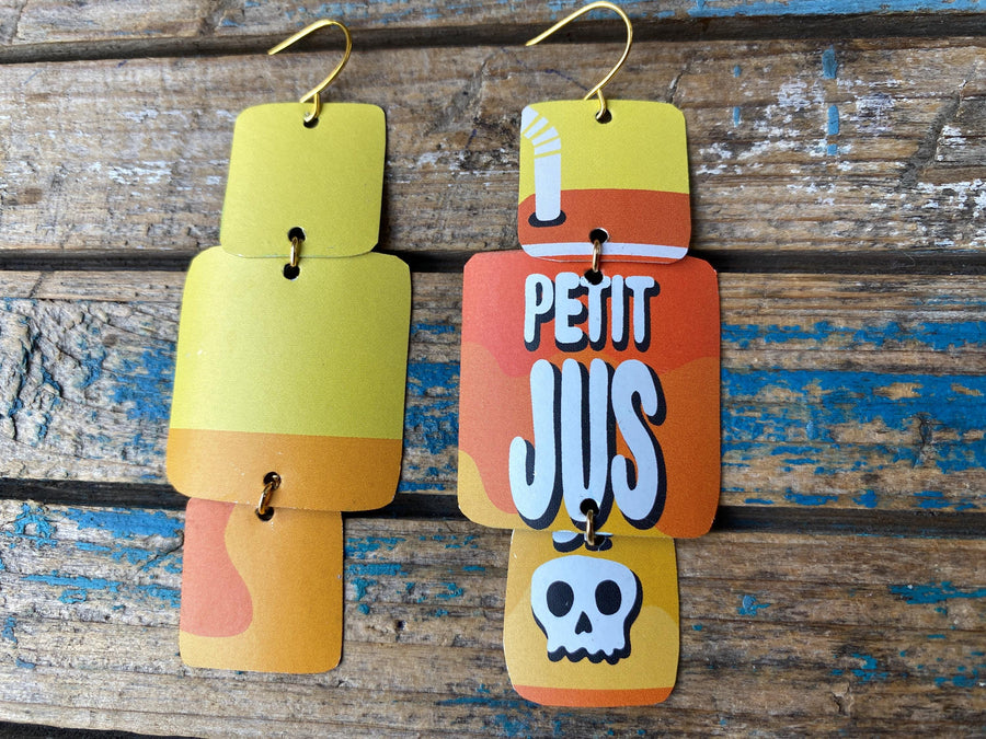 pair of yellow orange geometric earrings with text and skull design made from an upcycled beer can on a rustic wooden background