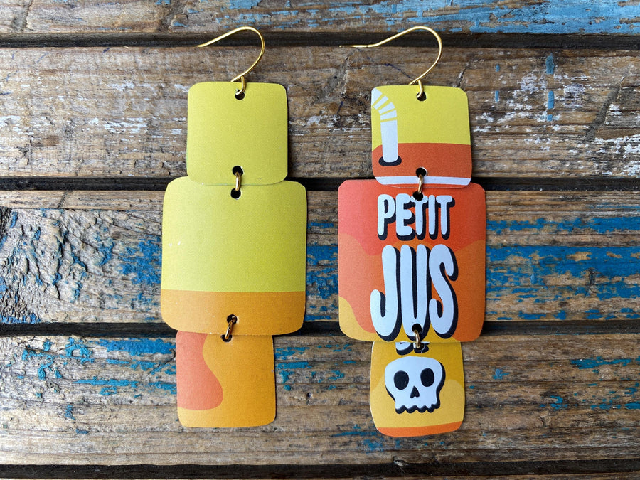 pair of yellow orange geometric earrings with text and skull design made from an upcycled beer can on a rustic wooden background