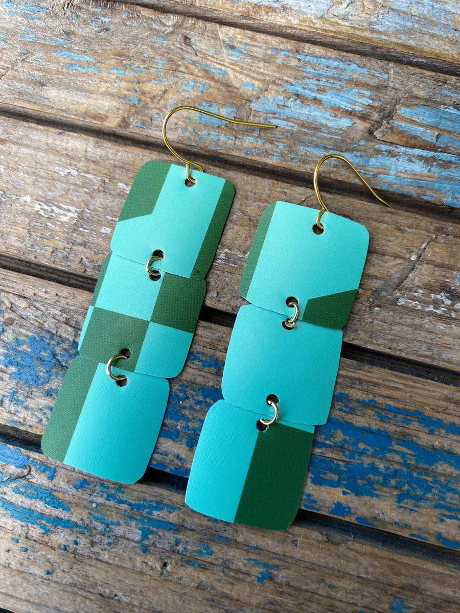 light and dark green coloured, geometric earrings made from a beer can, upcycled earrings on a rustic wooden background