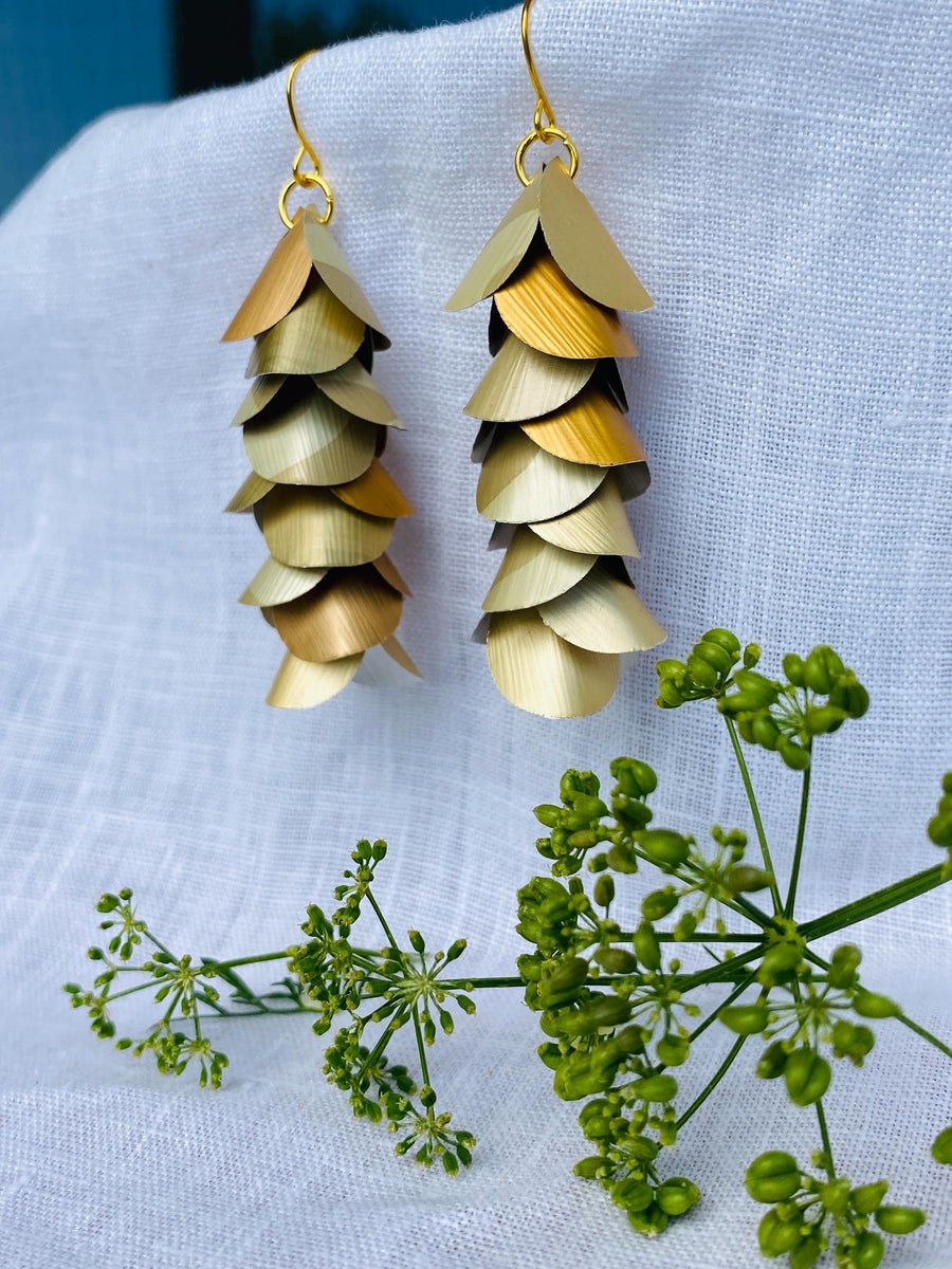 pair of creme-gold coloured, cascading earrings made from upcycled nespresso pod aluminium, on a white linen background and a little green flower