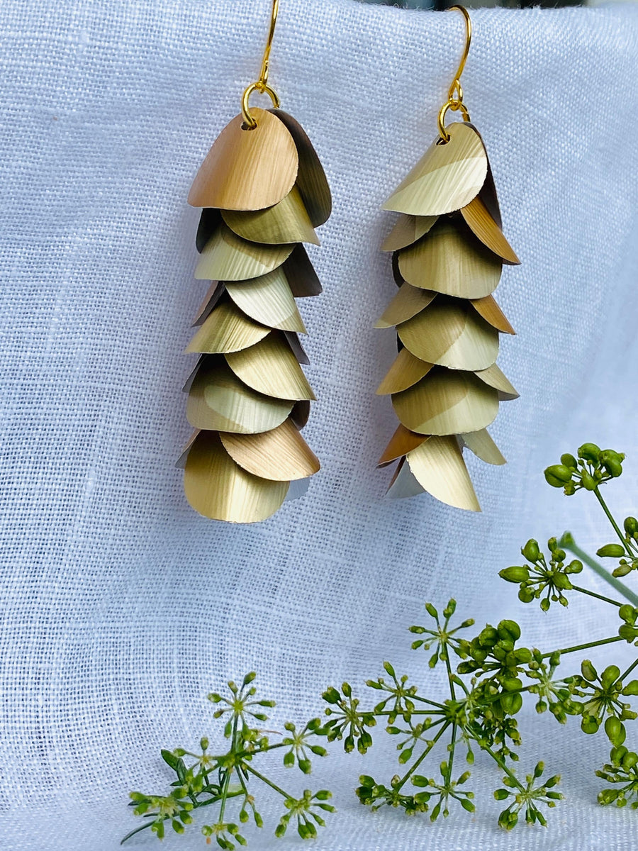 pair of creme-gold coloured, cascading earrings made from upcycled nespresso pod aluminium, on a white linen background and a little green flower