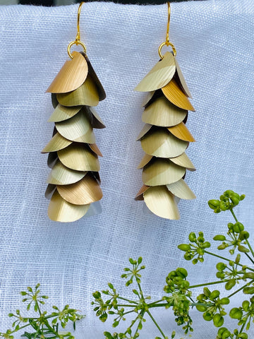 pair of creme-gold coloured, cascading earrings made from upcycled nespresso pod aluminium, on a white linen background and a little green flower
