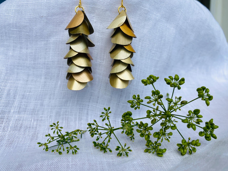 pair of creme-gold coloured, cascading earrings made from upcycled nespresso pod aluminium, on a white linen background and a little green flower