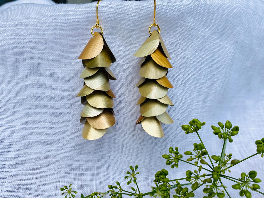 pair of creme-gold coloured, cascading earrings made from upcycled nespresso pod aluminium, on a white linen background and a little green flower