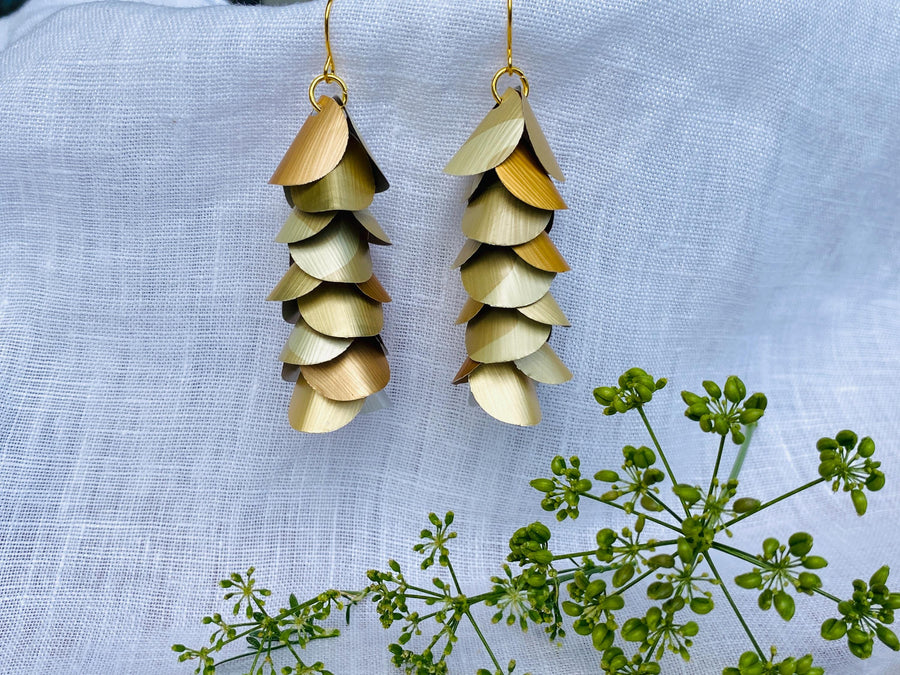 pair of creme-gold coloured, cascading earrings made from upcycled nespresso pod aluminium, on a white linen background and a little green flower