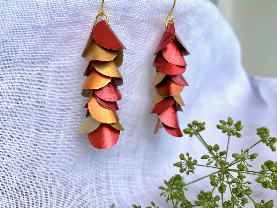 red orange gold cascade earrings made from upcycled nespresso capsule aluminium on a white linen background and green flower