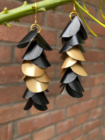 gold black cascade earrings made from upcycled nespresso capsules aluminium on a brick wall background