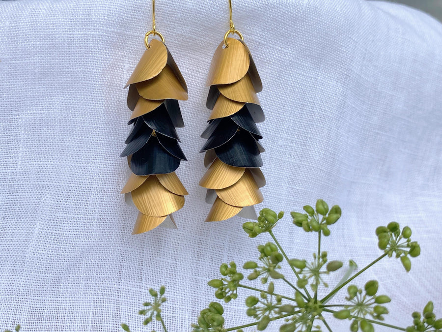 gold-black cascading earrings made from upcycled nespresso capsule aluminium on a white linen background and green flower