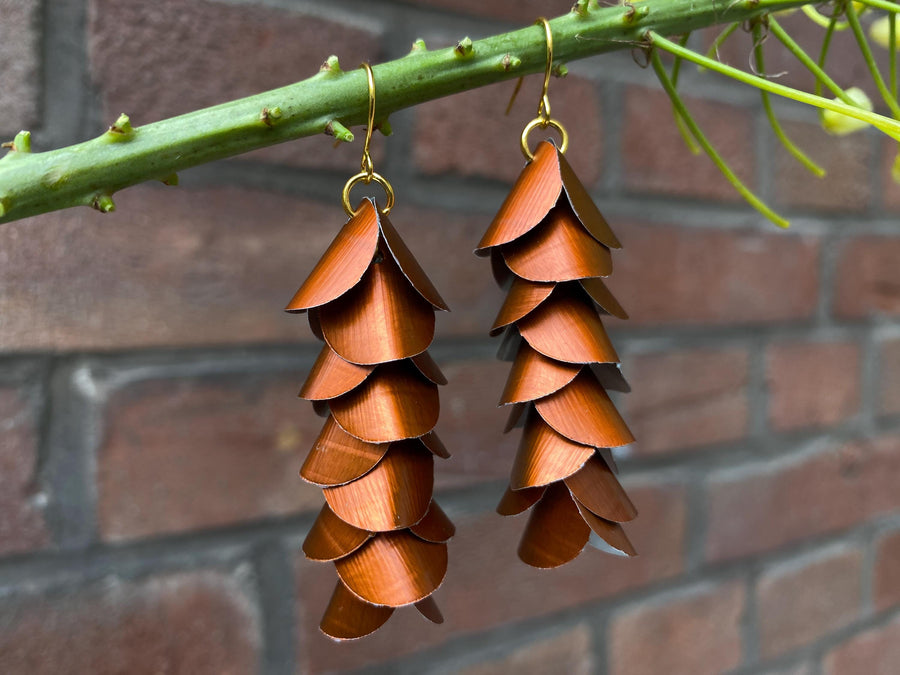 copper coloured cascade earrings made from upcycled nespresso capsule aluminium on a brick wall background