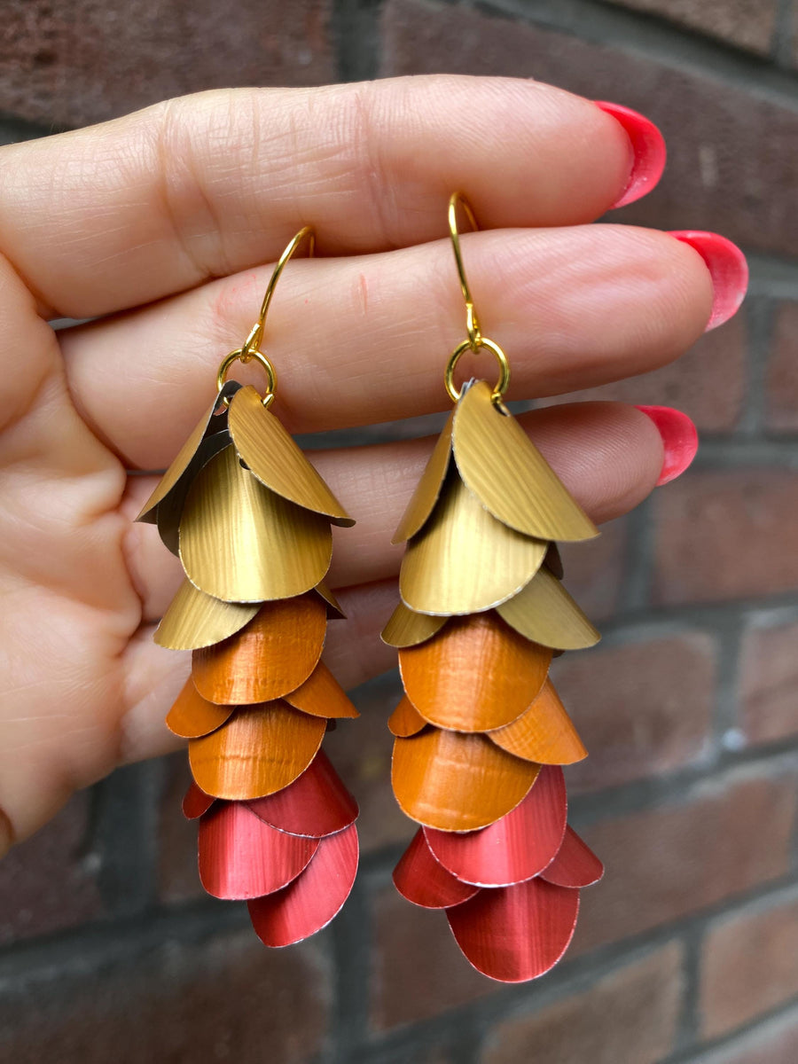 gold orange red cascade earrings made from upcycled nespresso capsules on a brick wall background