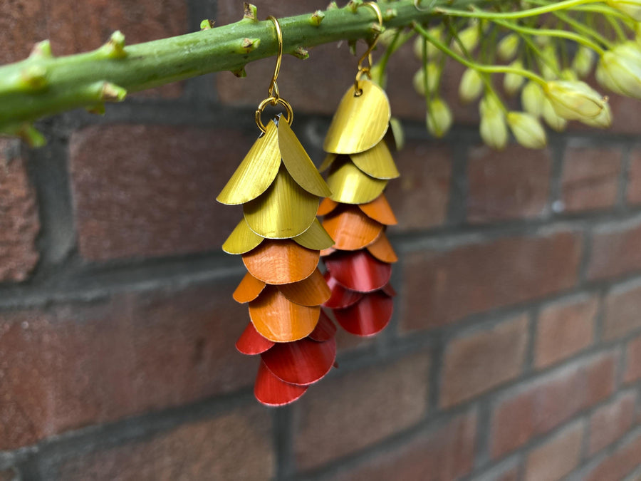 gold orange red cascade earrings made from upcycled nespresso capsules on a brick wall background