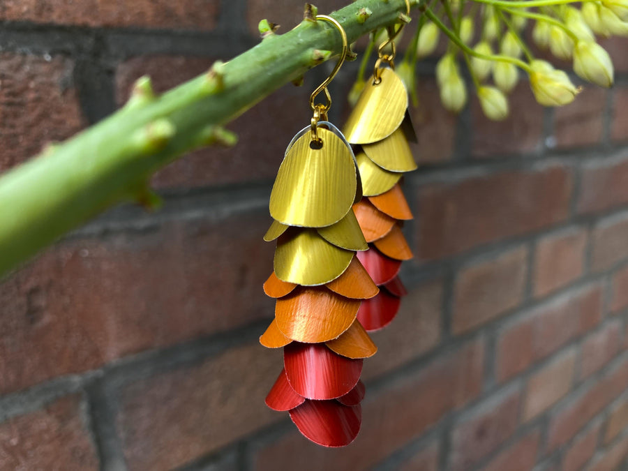 gold orange red cascade earrings made from upcycled nespresso capsules on a brick wall background