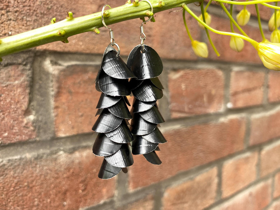 a pair of black, cascading aluminium earrings made from upcycled nespresso capsules on a brick wall background