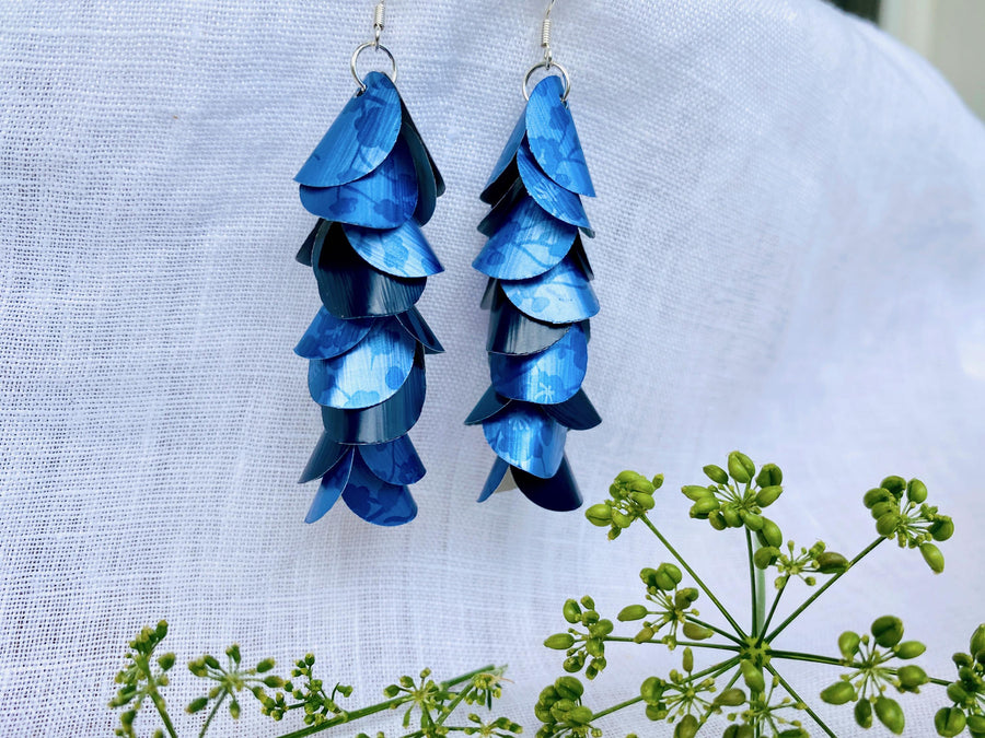 blue cascade earrings made from upcycled nespresso capsules aluminium on a white linen background and green flower