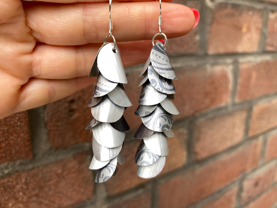 silver coloured cascade earrings made from upcycled nespresso capsules on a brick wall background