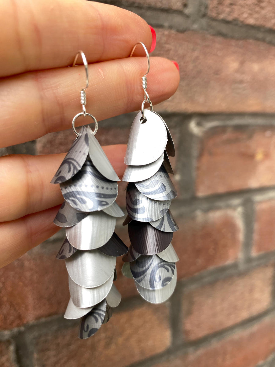 silver coloured cascade earrings made from upcycled nespresso capsules on a brick wall background
