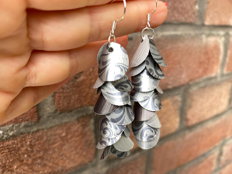 silver coloured cascade earrings made from upcycled nespresso capsules on a brick wall background