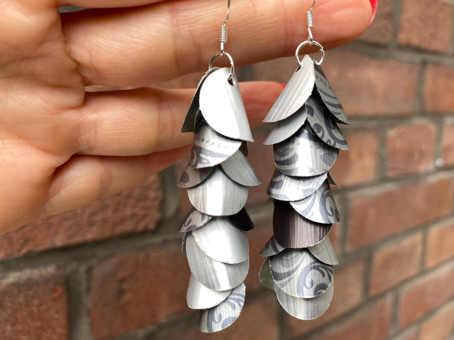 silver coloured cascade earrings made from upcycled nespresso capsules on a brick wall background