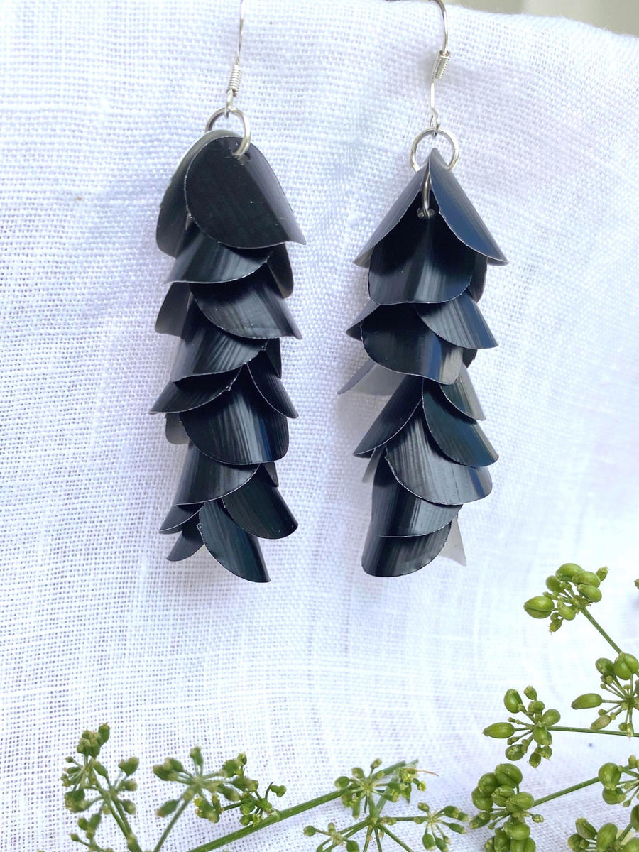 a pair of black, cascading aluminium earrings made from upcycled nespresso capsules on a white linen background and green flowers