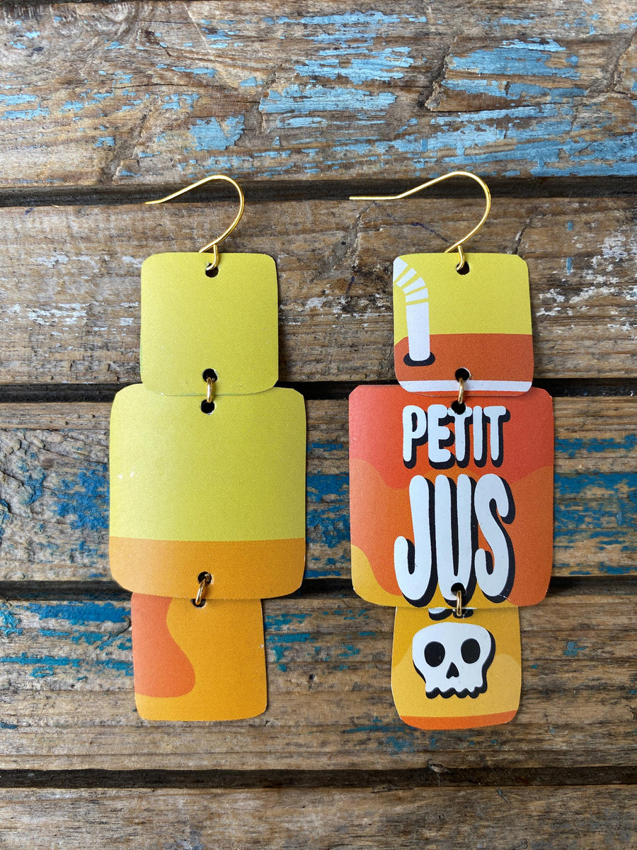 pair of yellow orange, asymmetric geometric earrings with text and skull design made from an upcycled beer can on a rustic wooden background