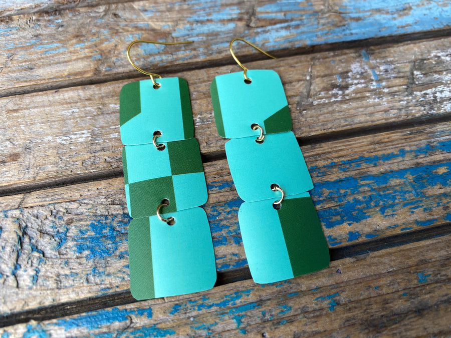 light and dark green coloured, geometric earrings made from a beer can, upcycled earrings on a rustic wooden background