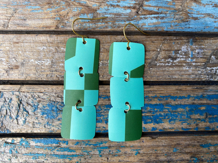 light and dark green coloured, geometric earrings made from a beer can, upcycled earrings on a rustic wooden background