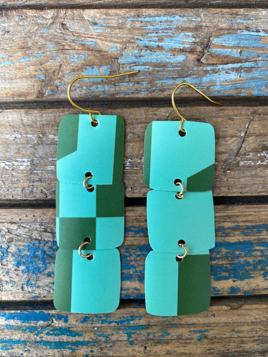 light and dark green coloured, geometric earrings made from a beer can, upcycled earrings on a rustic wooden background