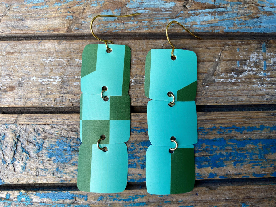 light and dark green coloured, geometric earrings made from a beer can, upcycled earrings on a rustic wooden background