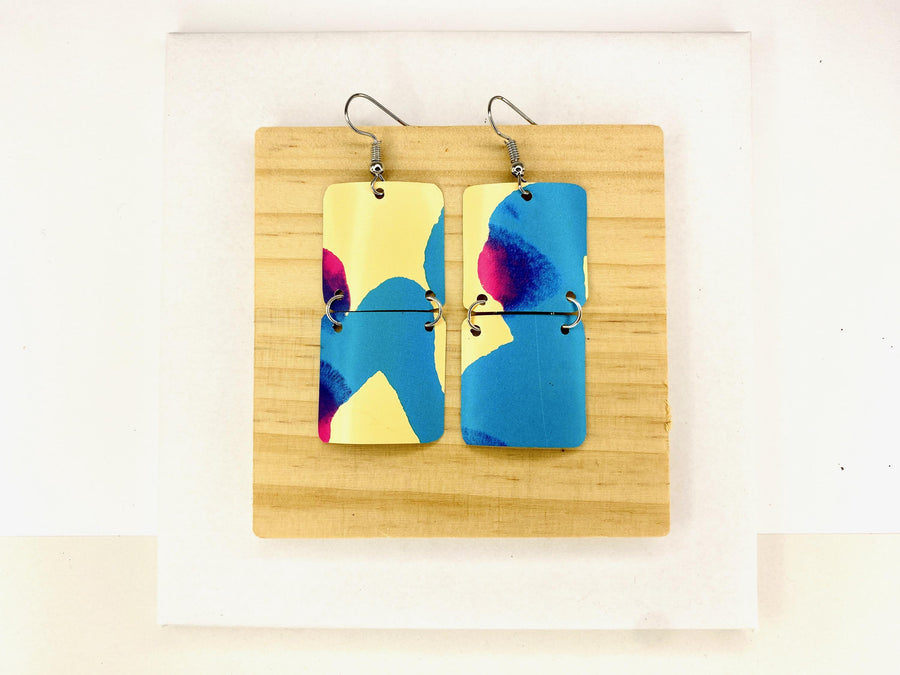 squared shape, abstract, upcycled earrings in blue, yellow, magenta colours made from a craft beer can,  on a wooden background