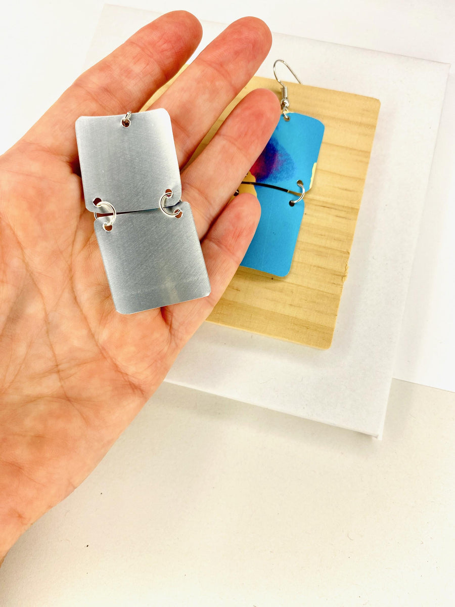 squared shape, abstract, upcycled earrings in blue, yellow, magenta colours made from a craft beer can displayed in hand