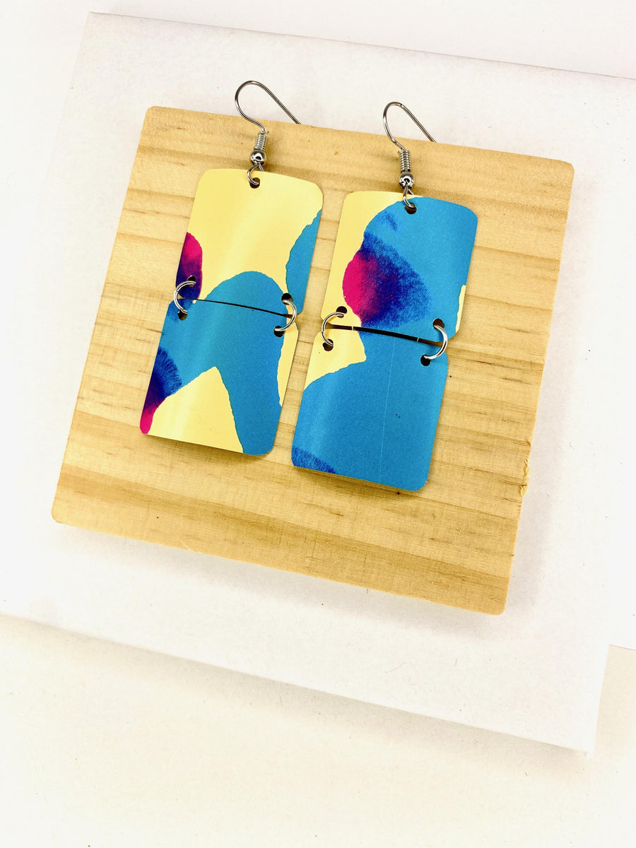 squared shape, abstract, upcycled earrings in blue, yellow, magenta colours made from a craft beer can,  on a wooden background