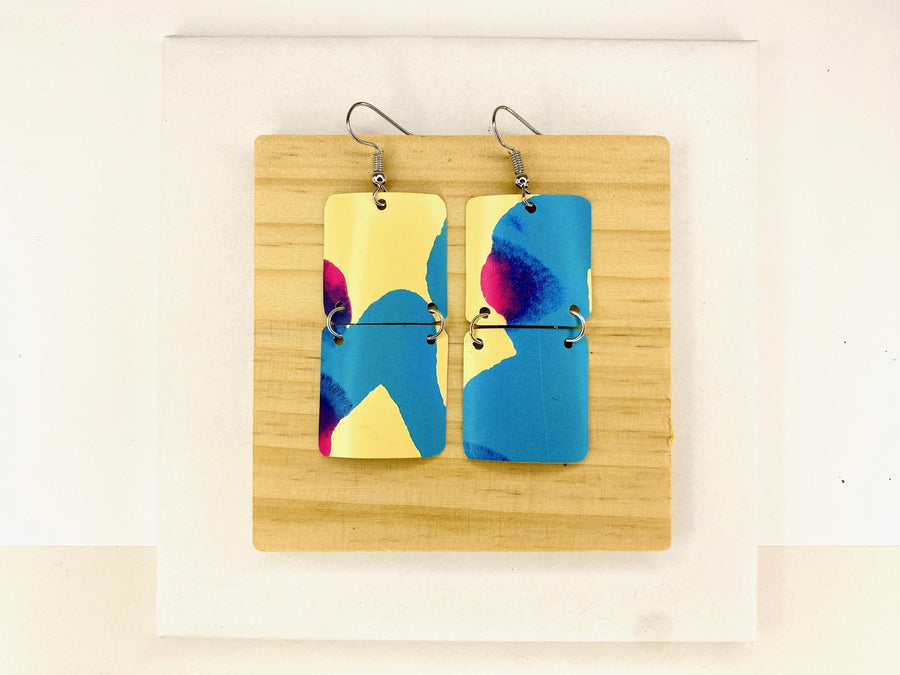 squared shape, abstract, upcycled earrings in blue, yellow, magenta colours made from a craft beer can,  on a wooden background