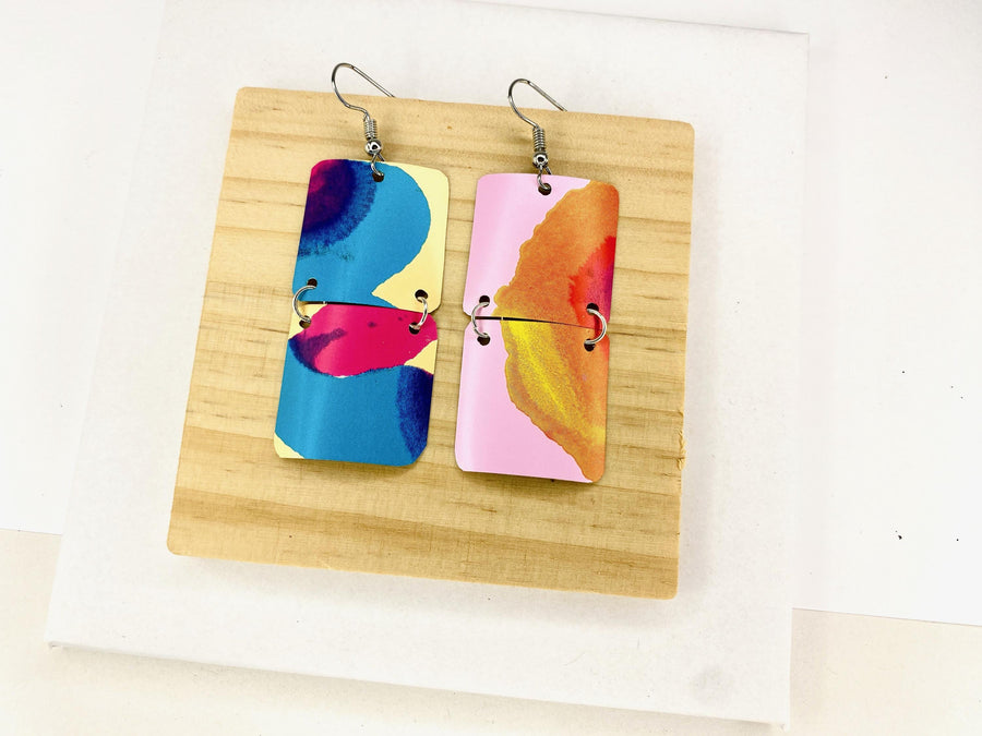 asymmetric, geometric earrings made from upcycled craft beer cans, in blue, yellow, magenta, orange and pink colours on a wooden and white background