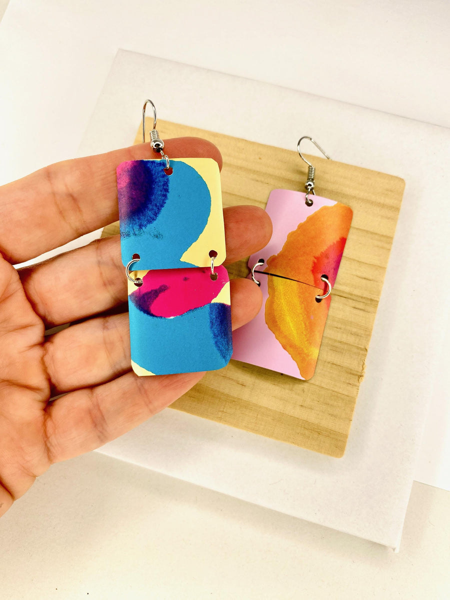 asymmetric, geometric earrings made from upcycled craft beer cans, in blue, yellow, magenta, orange and pink colours displayed in a hand