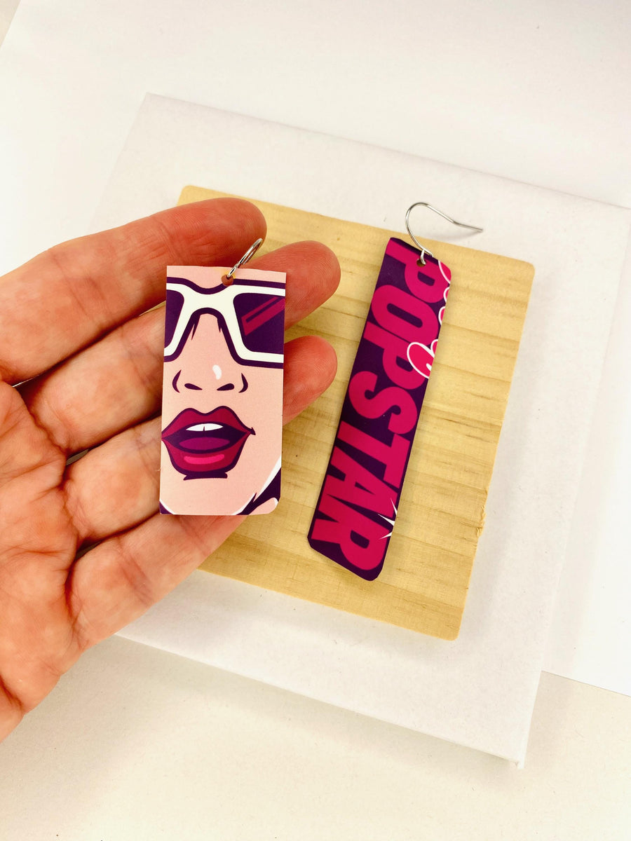 asymmetric, 90's Pop-art earrings featuring POPSTAR text and women's face made from  an upcycled craft beer can on a wooden and white background