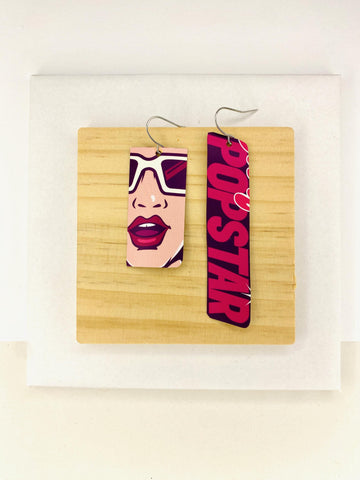 asymmetric, 90's Pop-art earrings featuring POPSTAR text and women's face made from  an upcycled craft beer can on a wooden and white background