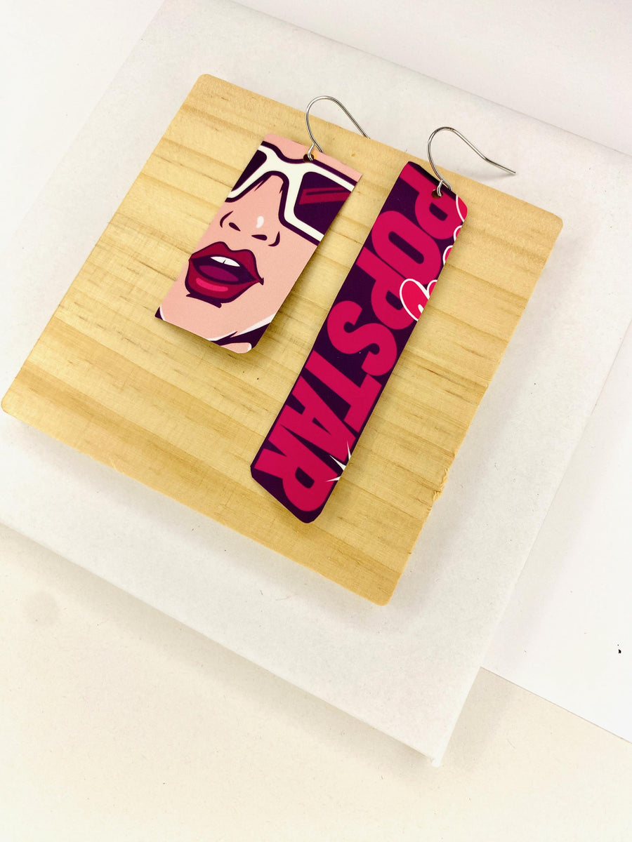 asymmetric, 90's Pop-art earrings featuring POPSTAR text and women's face made from  an upcycled craft beer can on a wooden and white background
