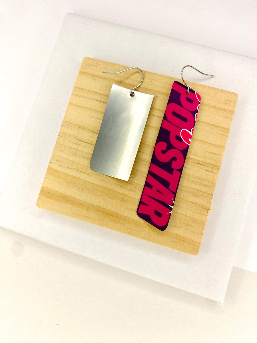 asymmetric, 90's Pop-art earrings featuring POPSTAR text and women's face made from  an upcycled craft beer can on a wooden and white background