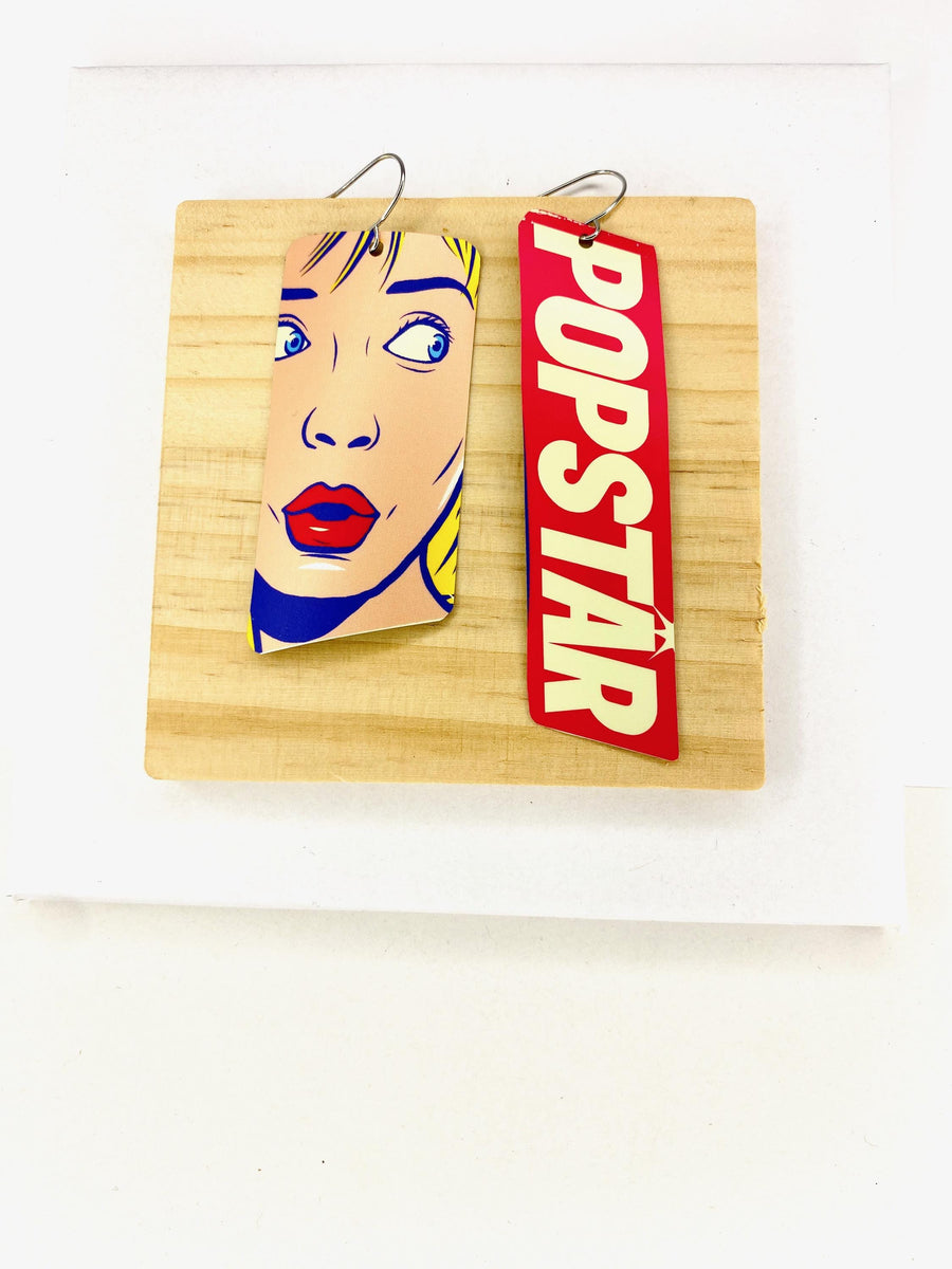 90s, disco, pop-art earrings featuring POPSTAR text and women's face in comic style on a wooden and white background