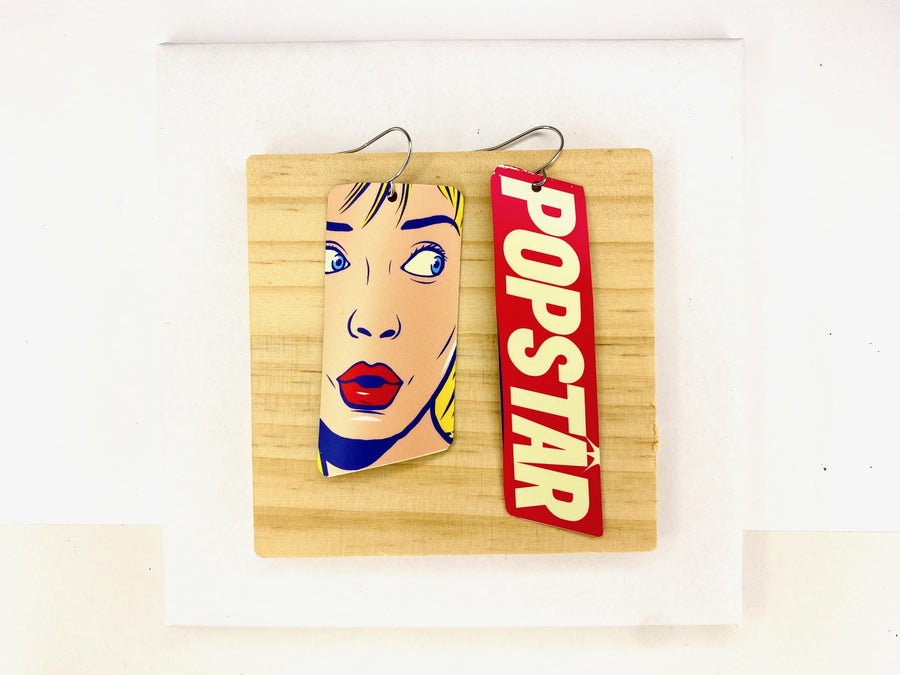 90s, disco, pop-art earrings featuring POPSTAR text and women's face in comic style on a wooden and white background