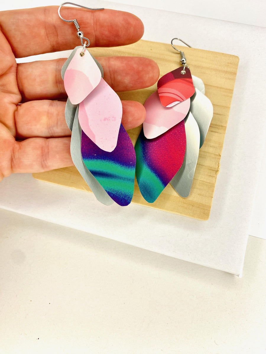 Pink purple green cascade earrings made from upcycled craft beer cans by Laura Zabo on a wooden and white background and displayed in hand