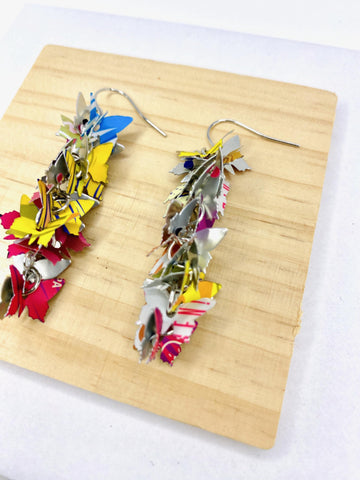 colourful, cascade statement earrings featuring tiny butterflies that are upcycled from craft beer cans on a wooden and white background